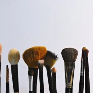 A variety of makeup brushes arranged vertically on a plain backdrop, perfect for beauty and cosmetic themes.