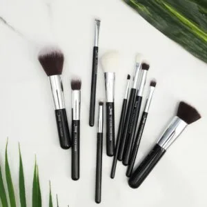 Flat lay of various makeup brushes on a marble surface with green leaves.