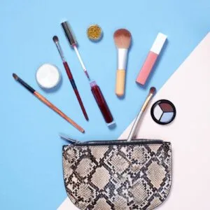 A flat lay of vibrant makeup items arranged around a stylish snakeskin cosmetic bag on a blue and beige background.